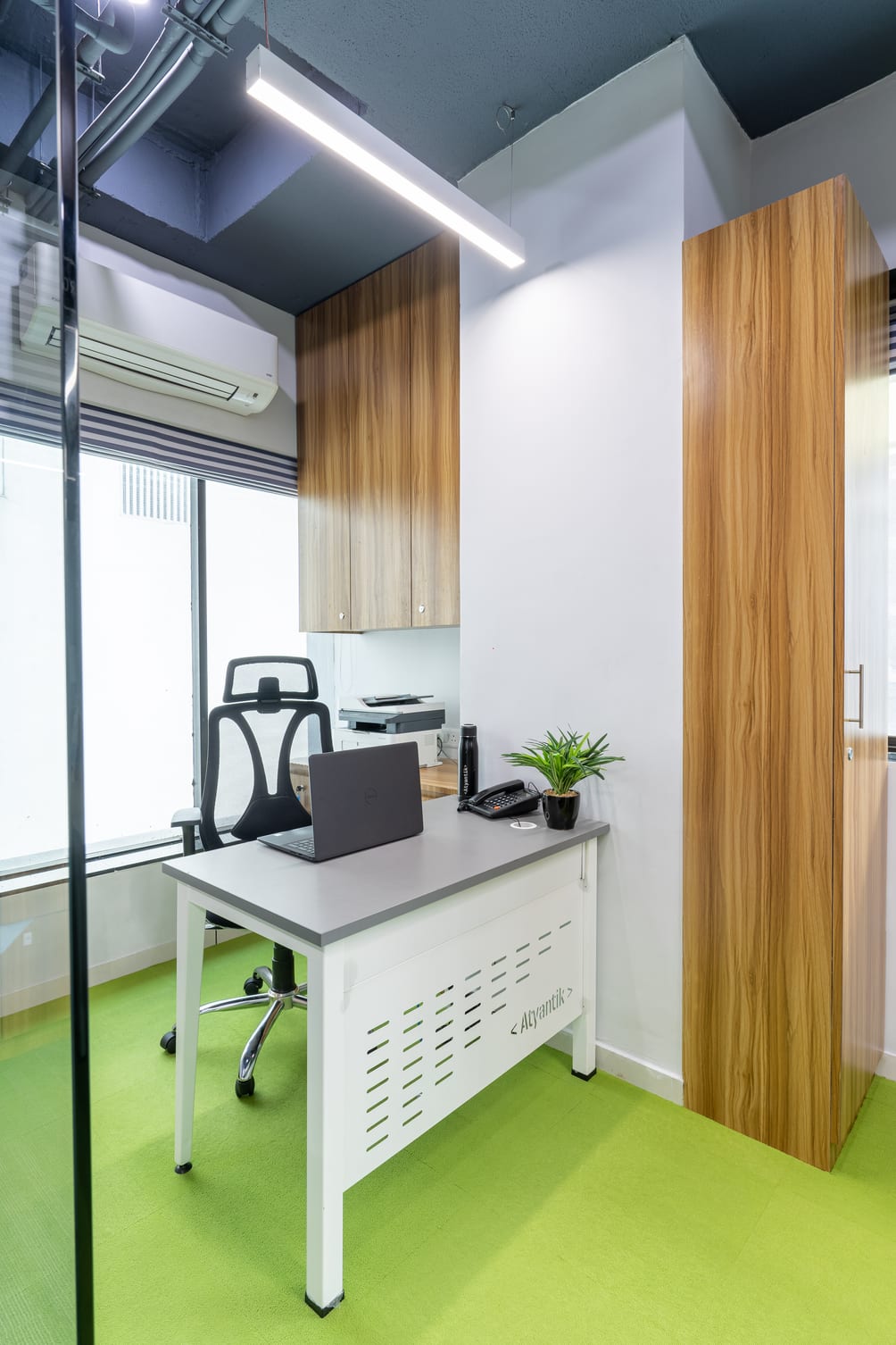 A small office cabin with a desk, laptop, printer and green flooring